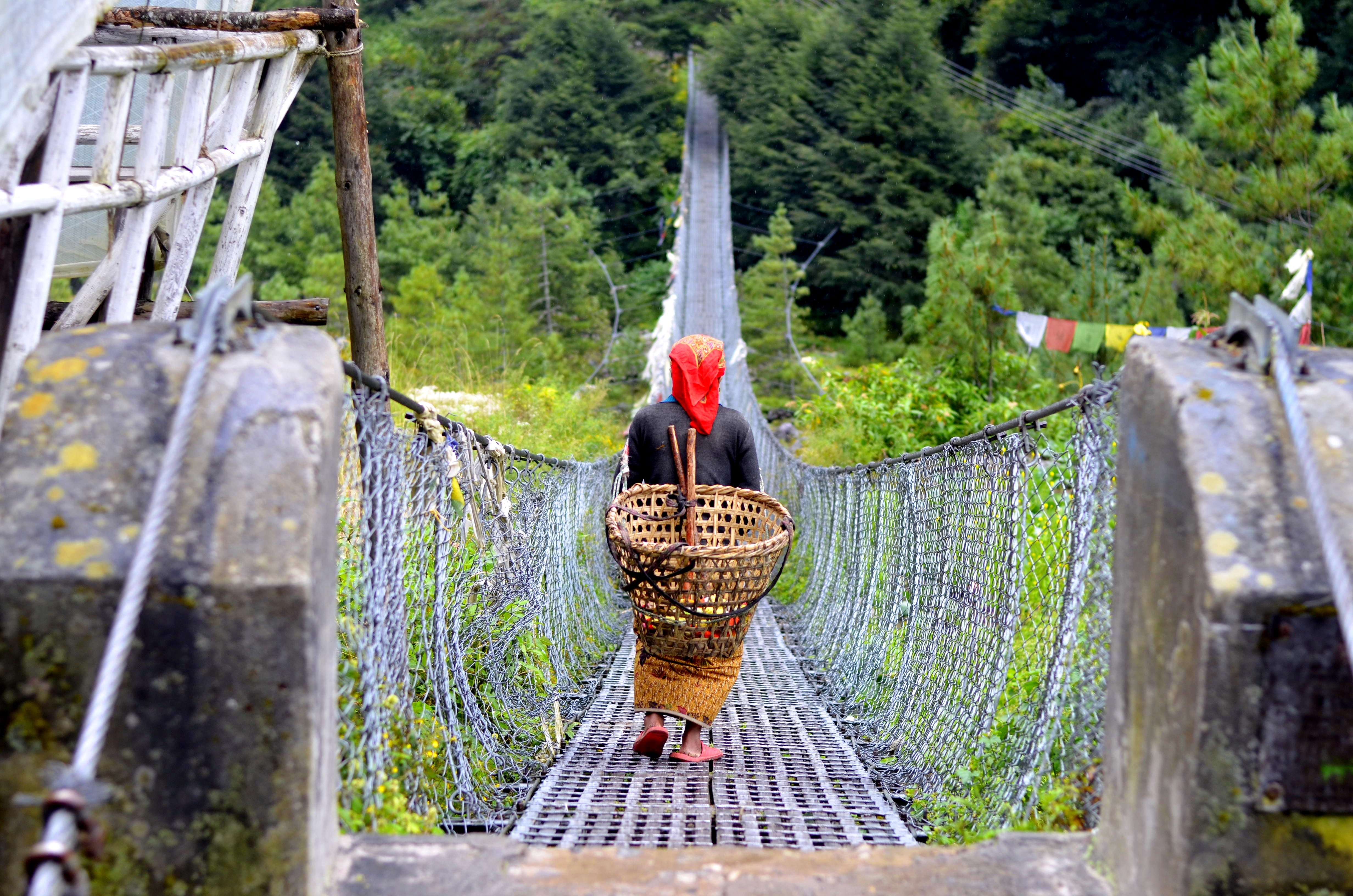 A woman carries a basket across a bridge