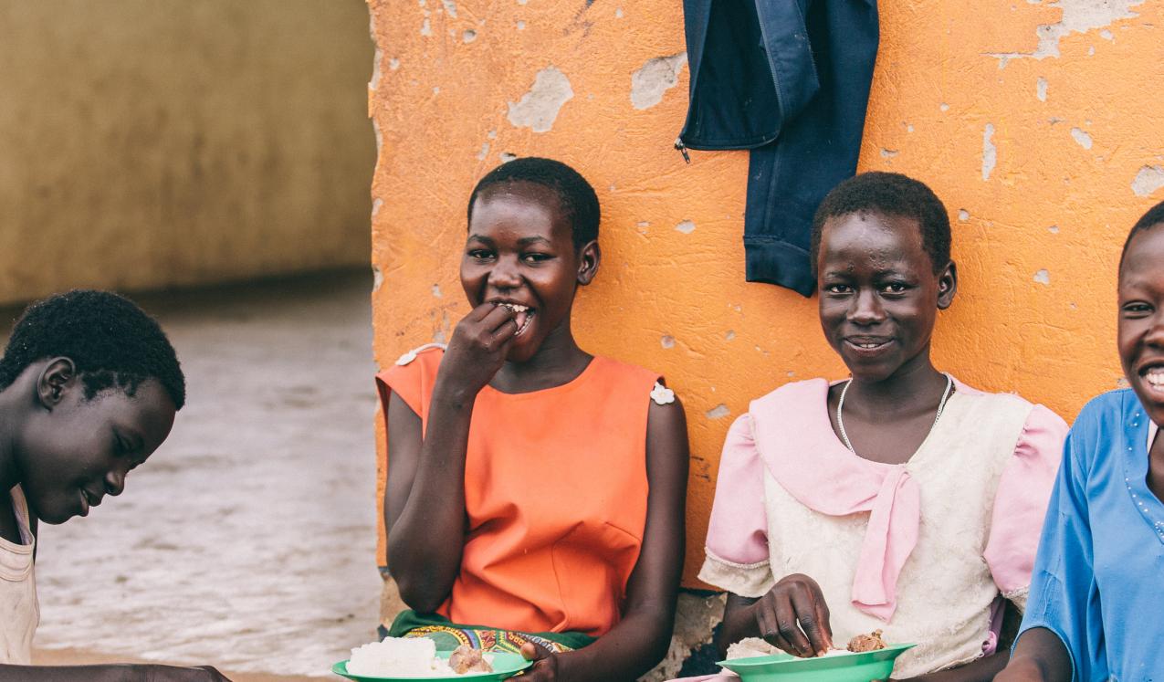 Lucy Agweto (far left), Christine Akwaso (far right), and their peers enjoy a meal together in Oditel, Uganda. © Brian Wolfe