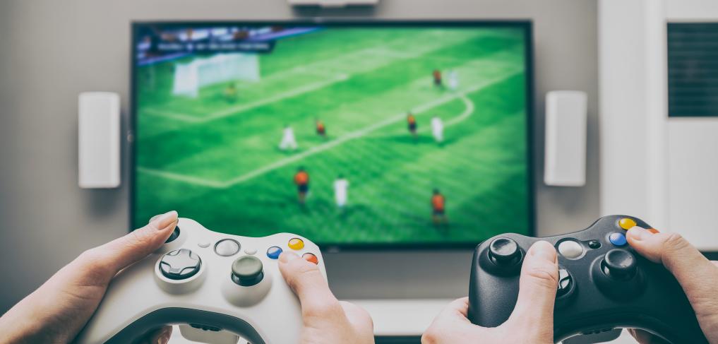 Hands operating video game controllers playing a football-base game. © REDPIXEL/shutterstock 537529714