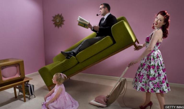 A woman vacuums whilst a man reads his been. Copyright Getty images