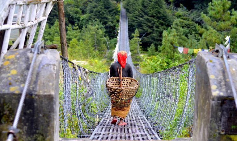 A woman carries a basket across a bridge