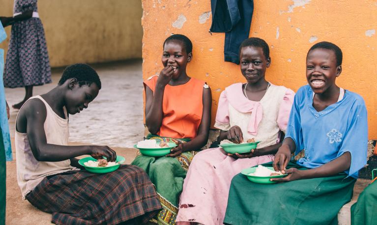 Lucy Agweto (far left), Christine Akwaso (far right), and their peers enjoy a meal together in Oditel, Uganda. © Brian Wolfe