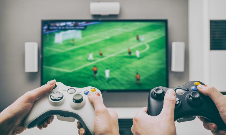 Hands operating video game controllers playing a football-base game. © REDPIXEL/shutterstock 537529714