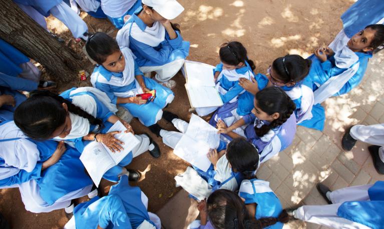 Schoolgirls at an Aahung partner school reading in the shade of a tree. © Aahung