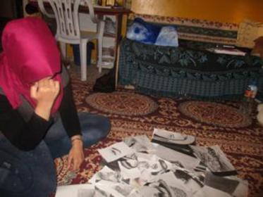 A girl sits on the floor with her face covered