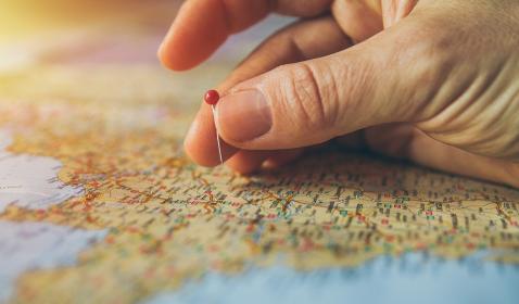 A hand putting a pin in a map.