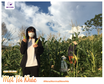 A woman wearing a mask holding up corn in a field. © Vo Von Tan for He Can/WISE Vietnam