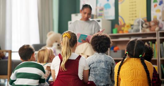 A kindergarten with children and teacher reading a story © PeopleImages | Shutterstock ID: 2472680051