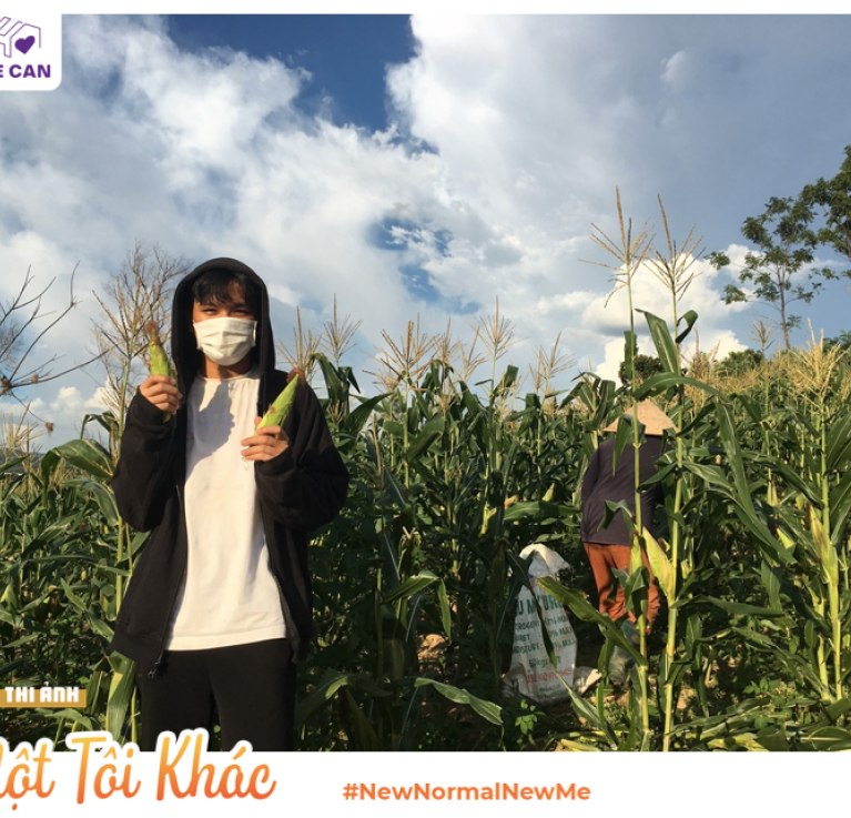 A woman wearing a mask holding up corn in a field. © Vo Von Tan for He Can/WISE Vietnam