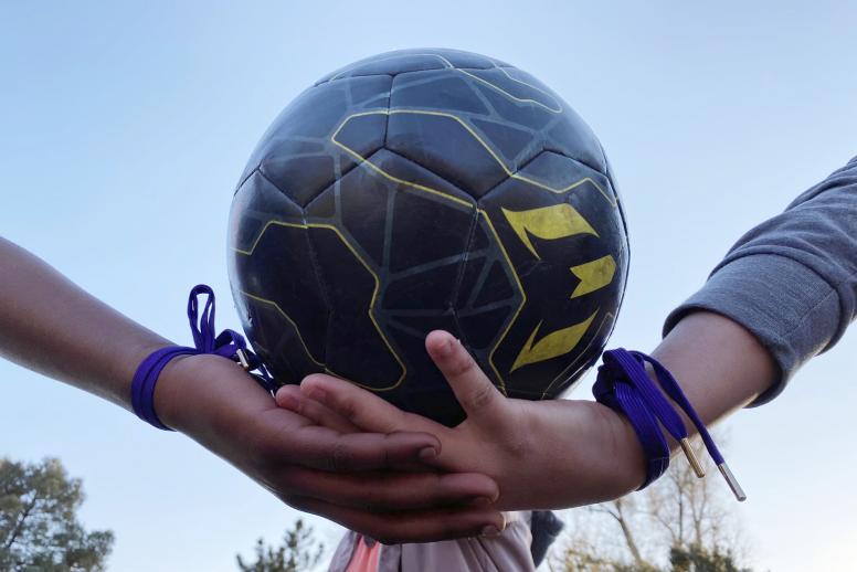 A close-up of a football with two players with matching bracelets holding it. ©Soccer Without Borders