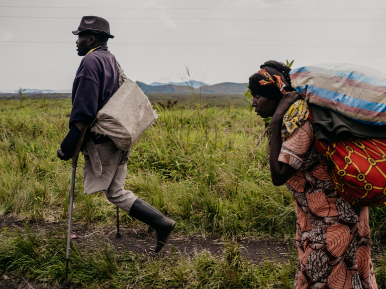 A disabled man and a woman carrying belongings flee ongoing M23 attacks as artillery and attack aircraft can be heard behind them, Sake, South Kivu Province, DRC, February 2024. © Hugh Kinsella Cunningham.
